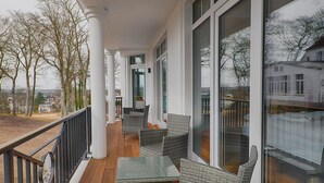 Un balcon doté de meubles en osier, de grandes fenêtres et offrant une vue sur les environs.