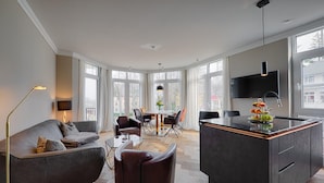 Un salon moderne comprenant un canapé, des fauteuils, une table à manger et un îlot de cuisine.