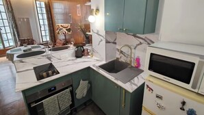 Una cucina con piano di lavoro in marmo, lavello, forno a microonde e mobili verdi.