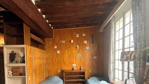 Una stanza con due letti singoli, pareti in legno, una finestra con tende e uno scaffale con diversi oggetti.
