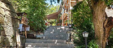 A set of stone steps leading up to a wooden structure with a roof, surrounded by trees and greenery.