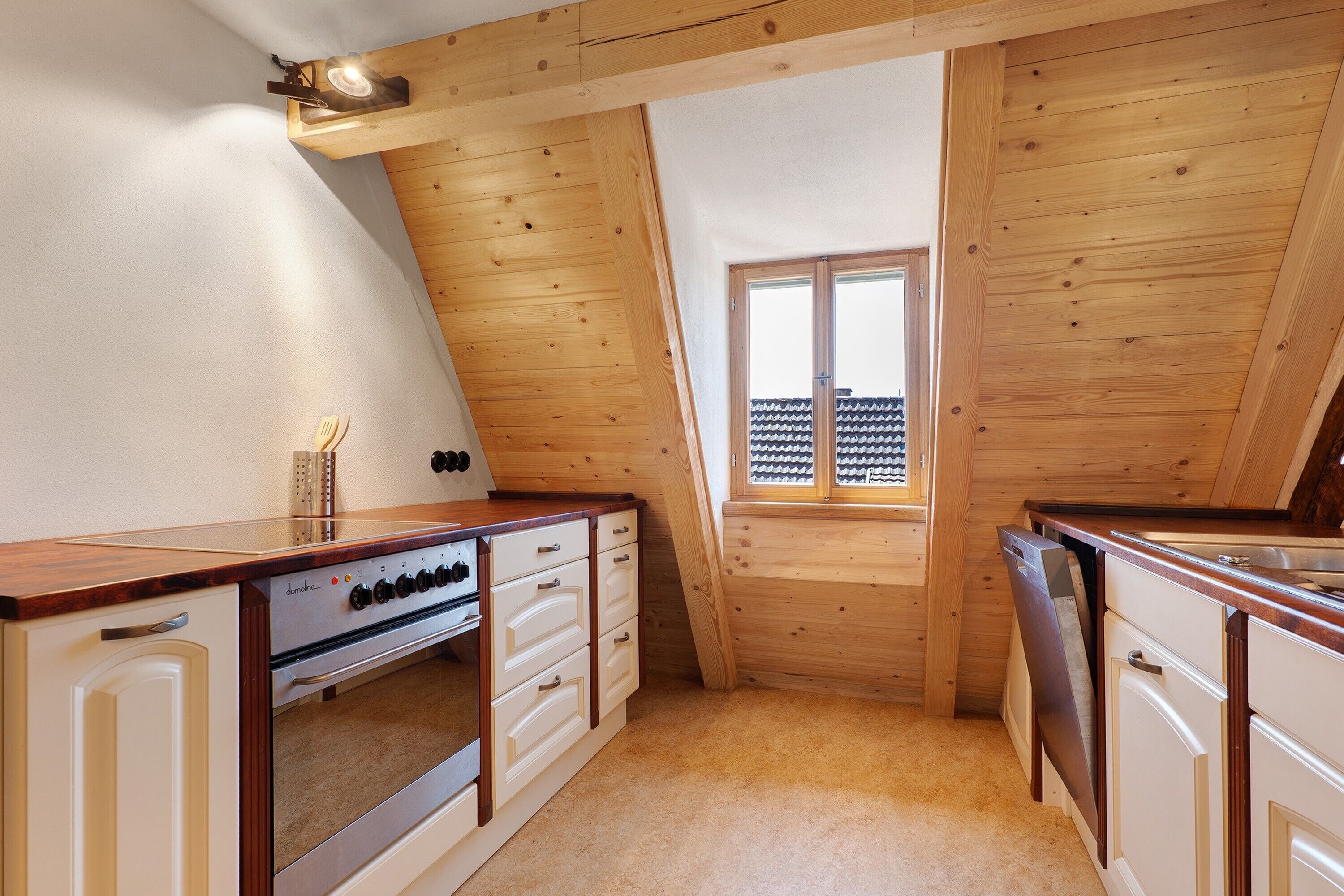 Una cucina compatta con pareti in legno, un piano cottura integrato e una finestra con vista su un balcone.