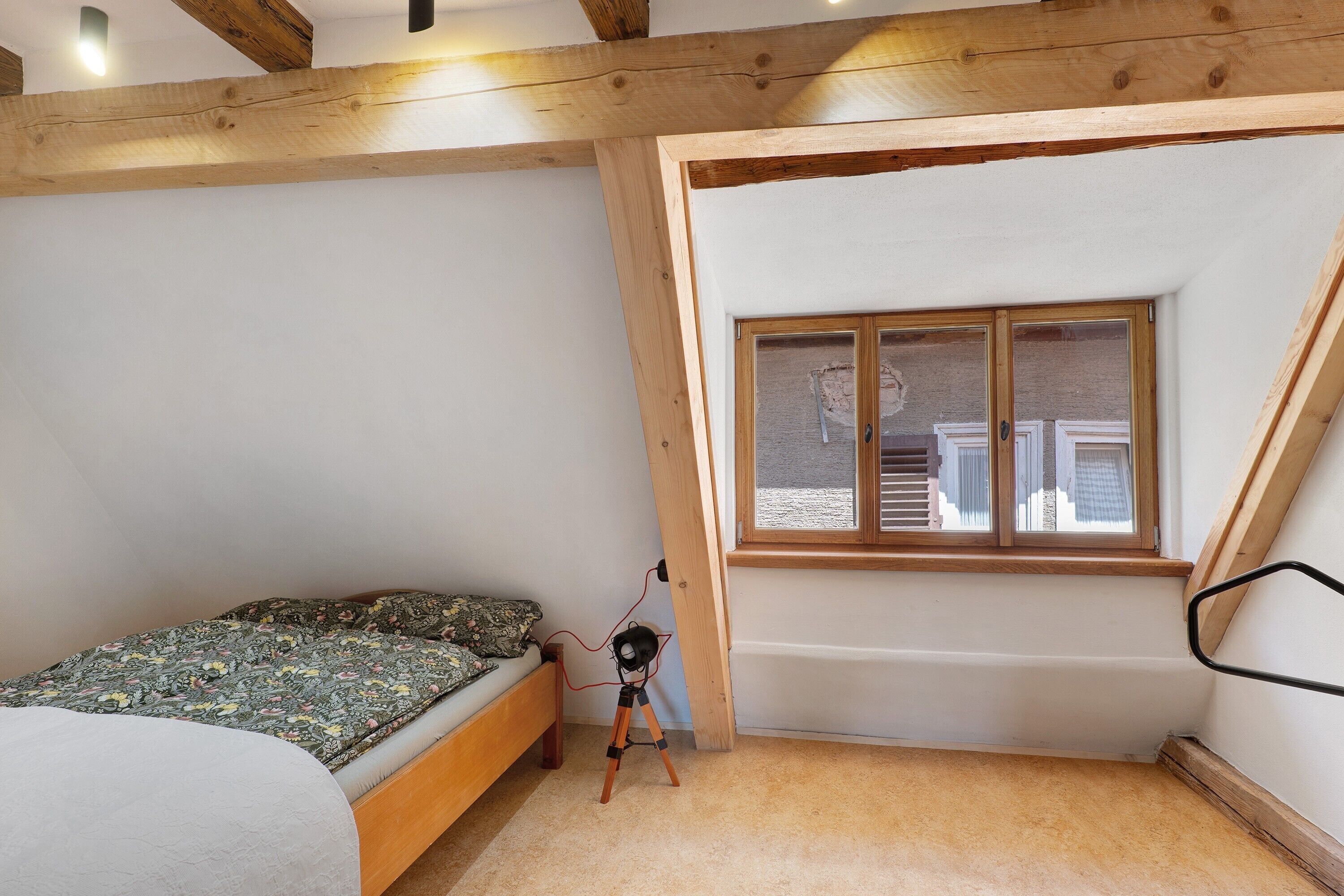 Ein Schlafzimmer mit einem Einzelbett, einem Fenster und einer Holzbalkendecke.