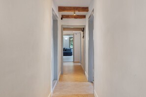Un pasillo estrecho con una viga de techo de madera que conduce a una habitación con un sofá azul y una ventana.