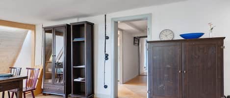Een kamer met een eettafel, stoelen, een kast en een deur naar een andere kamer.