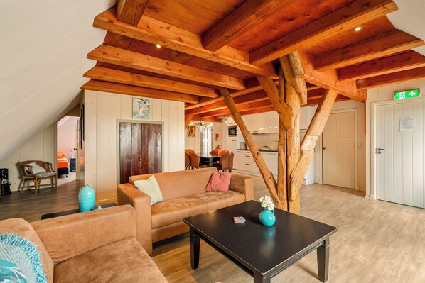 Ein gemütlicher Wohnbereich mit Holzbalkendecke, einer Couch, einem Couchtisch und einem Essbereich im Hintergrund.