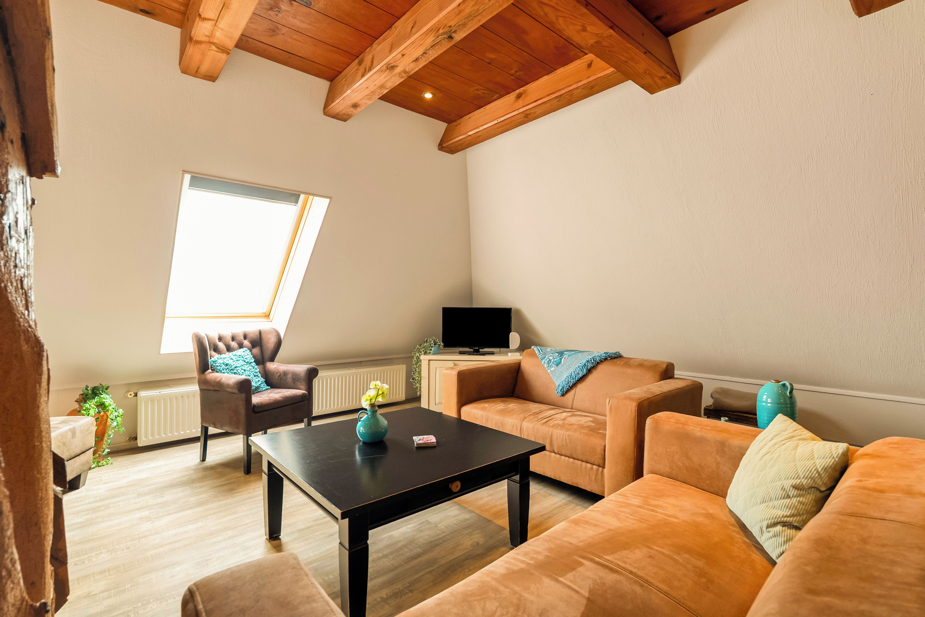 Een woonkamer met een hoge plafond, een bank, een fauteuil, een salontafel en een televisie.