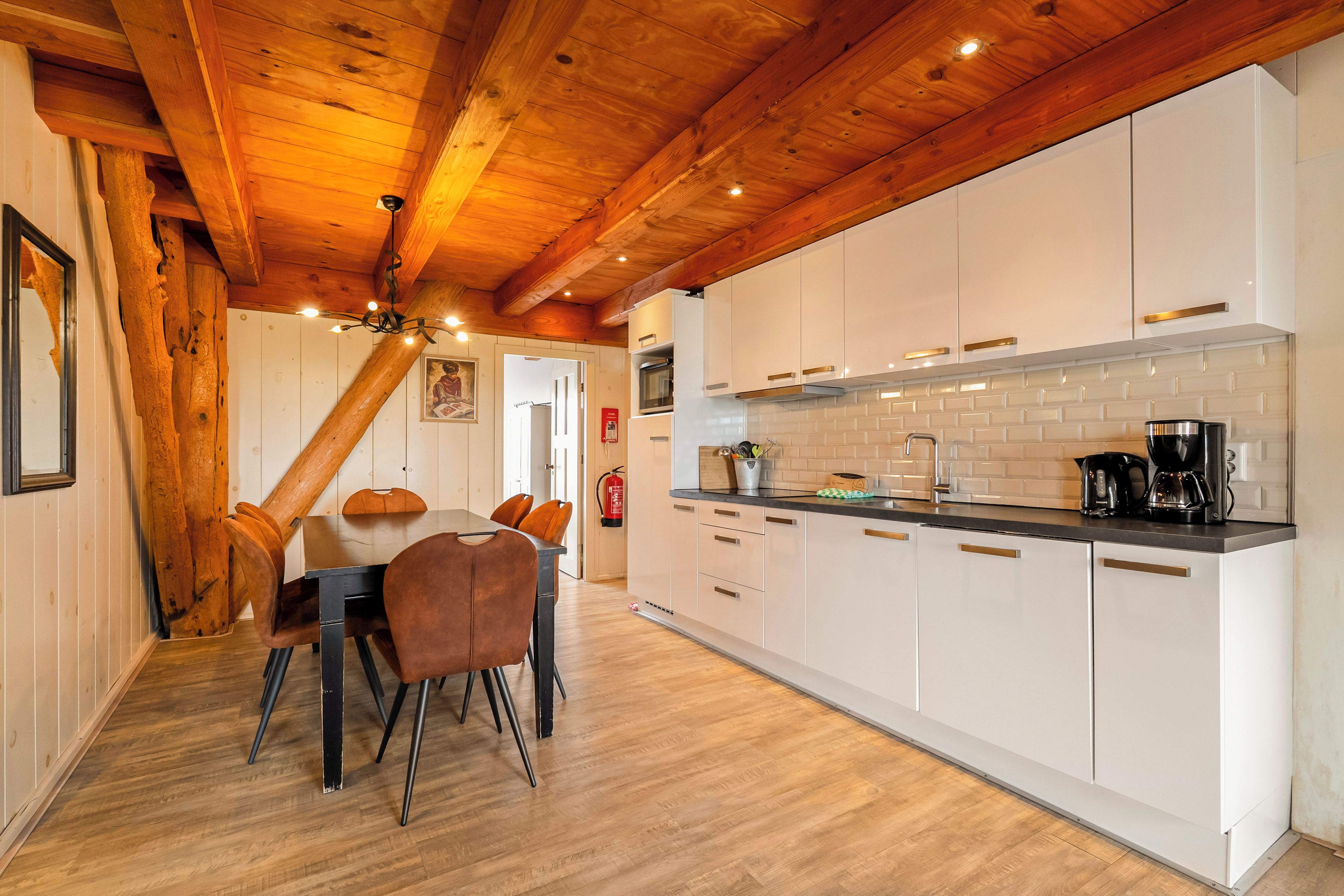 Een moderne keuken met witte kasten, een zwart aanrecht en een houten plafond.