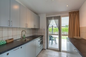 A modern kitchen with a sink, stove, and cabinets, leading to a patio with a table and chairs. - Beautiful detached holiday bungalow at Duinland holiday park in Sint Maartenszee with a fully enclosed garden! (Sint Maartensvlotbrug)