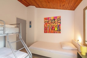 A bunk bed with a lower bunk, a single bed with a pillow, a painting on the wall, and a bedside lamp. - A beautiful, detached vacation bungalow in Park Duinland in Sint Maartenszee with a fully fenced-in yard! (Sint Maartensvlotbrug)