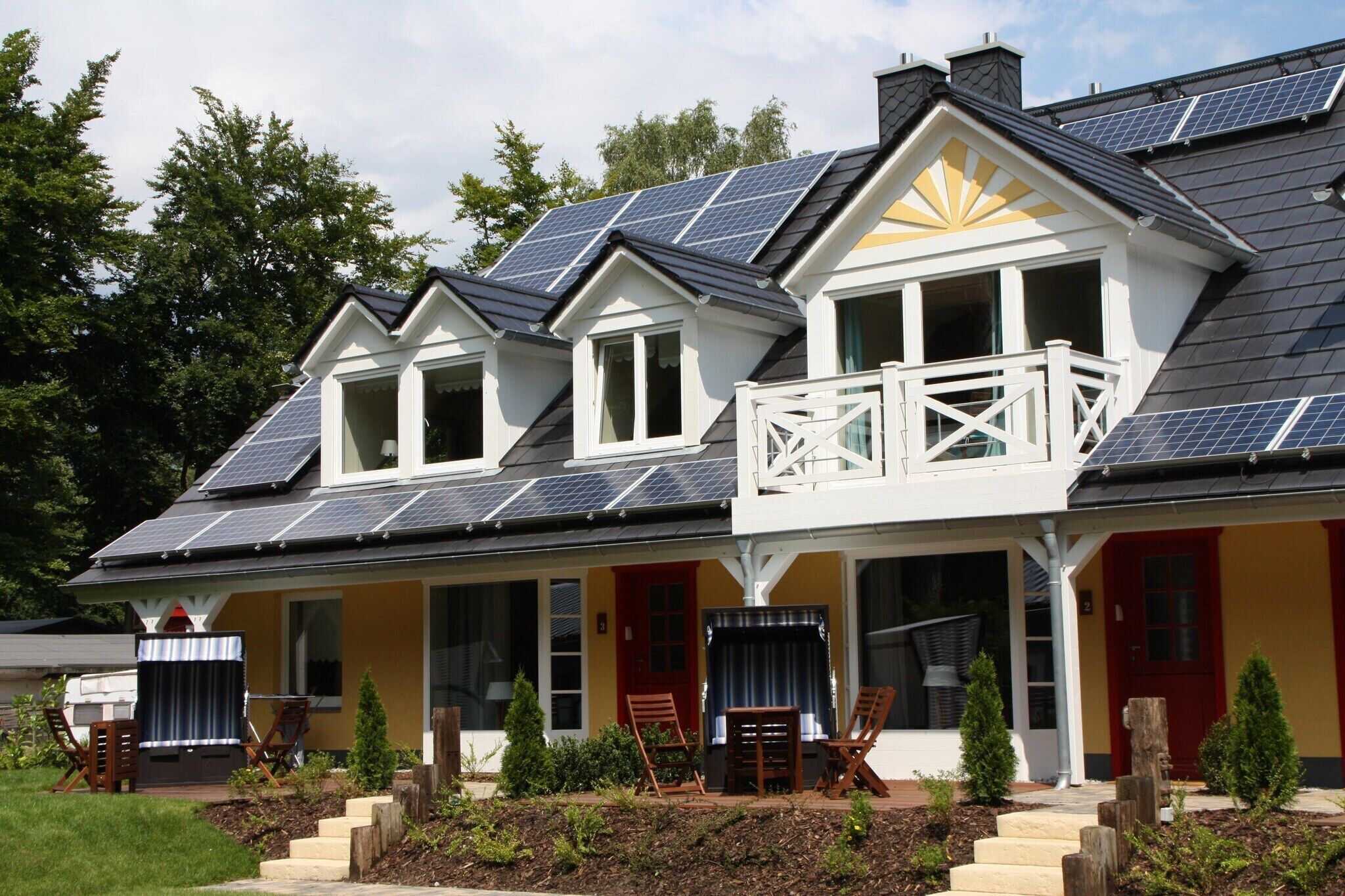 Ein zweistöckiges Haus mit Solaranlage, einem Balkon und einer Veranda mit Stühlen.