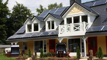 Ein zweistöckiges Haus mit Solaranlage, einem Balkon und einer Veranda mit Stühlen.