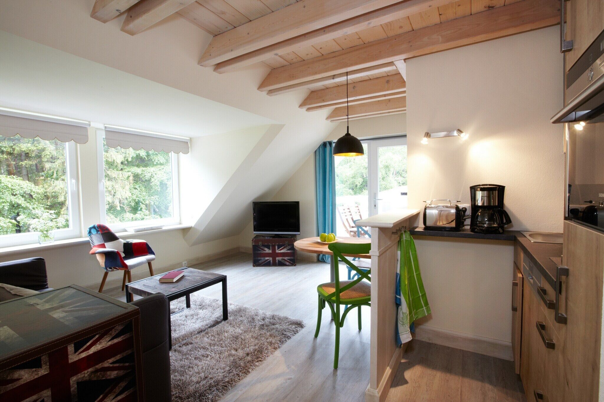 Ein Loft-Zimmer mit Essbereich, Küche und großem Fenster mit Blick auf Grünflächen.