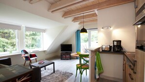 Een loft-achtige kamer met een eethoek, keuken en een groot raam met uitzicht op groen.