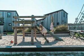 A playground with a slide and climbing structure, surrounded by sandy ground and wooden buildings. - Perfect for kids! (Callantsoog)