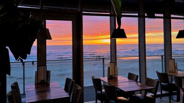 En interiörbild från en restaurang med stora fönster som vetter mot havet vid solnedgången.