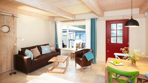 Una sala de estar acogedora con un sofá marrón, una mesa de centro de madera, una puerta roja y un comedor con mesa y sillas.