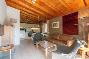 Ein gemütlicher Wohnbereich mit Holzbalkendecke, einer Couch, einem Couchtisch und einer Küche im Hintergrund.
