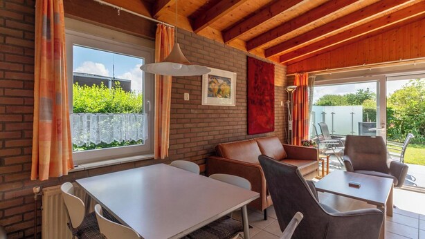 A dining area with a table and chairs, a bench, and a view through a glass door to an outdoor space. - Cozy, well-furnished vacation bungalow with a sunny, green garden (Callantsoog)