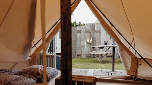 A tent with a bed inside, a wooden table outside, and a wooden fence in the background. - Unique accommodation (Callantsoog)
