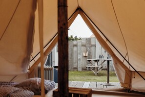 Una tenda con un letto all'interno, un tavolo di legno all'esterno e una recinzione di legno sullo sfondo.