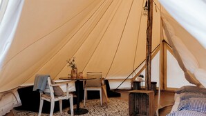 A tent interior with a table, chairs, a patterned rug, and a bed with checkered bedding. - Unique accommodation (Callantsoog)