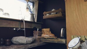 A rustic kitchen with a wooden counter, a hanging pot rack, a kettle, and a colander. - Unique accommodation (Callantsoog)