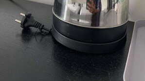 A kettle on a black countertop with a power cord plugged into a wall socket.