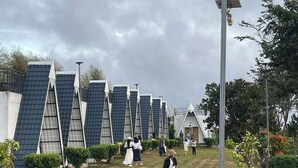 A row of modern, triangular-roofed buildings with a central walkway and greenery.