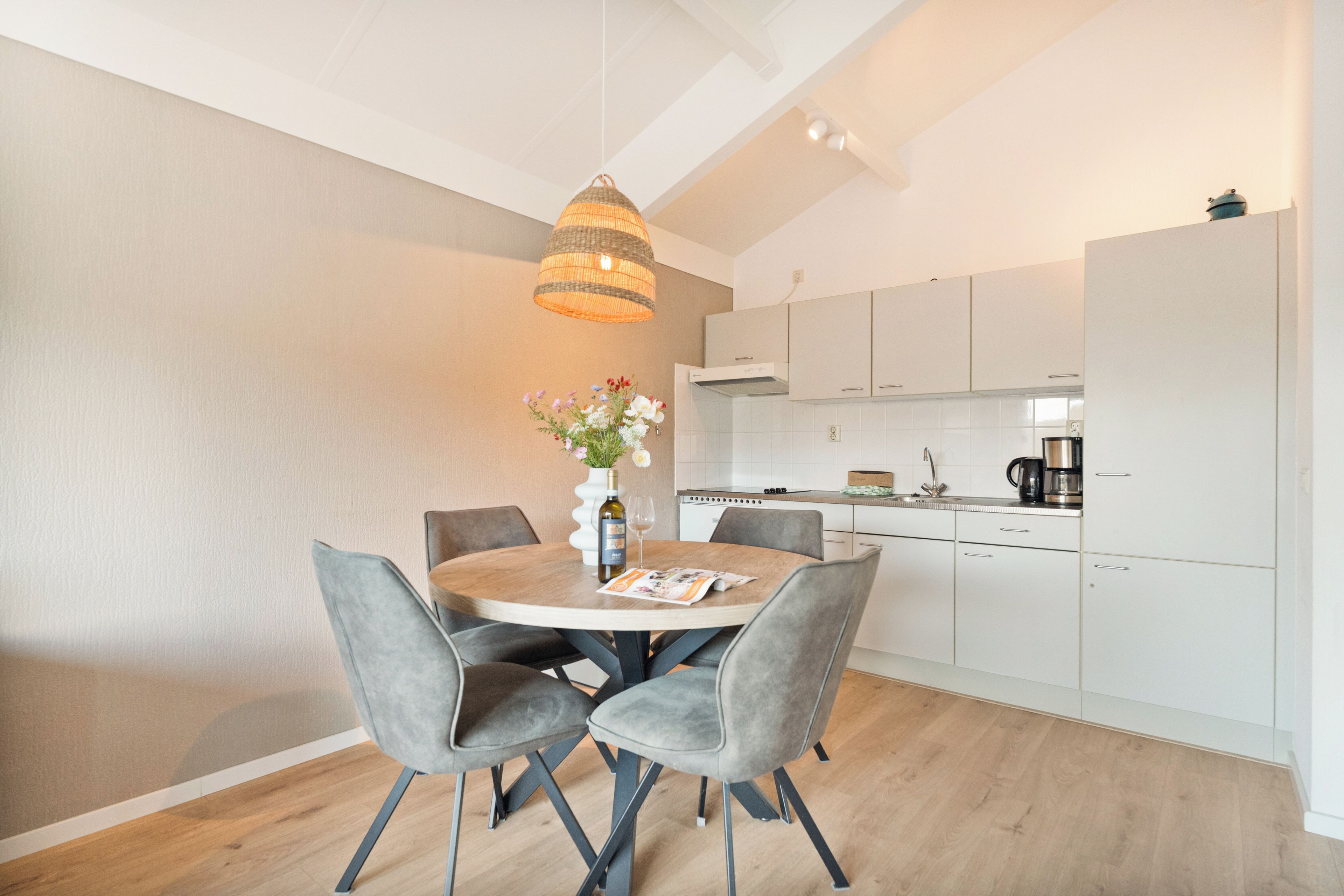 A modern kitchen with white cabinets, a dining table with four chairs, and a hanging light fixture.