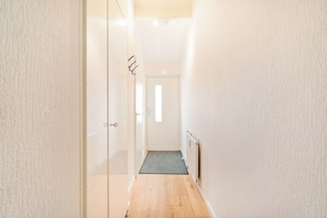 Ein schmaler Flur mit Holzboden, der zu einer Tür mit kleinem Fenster führt.