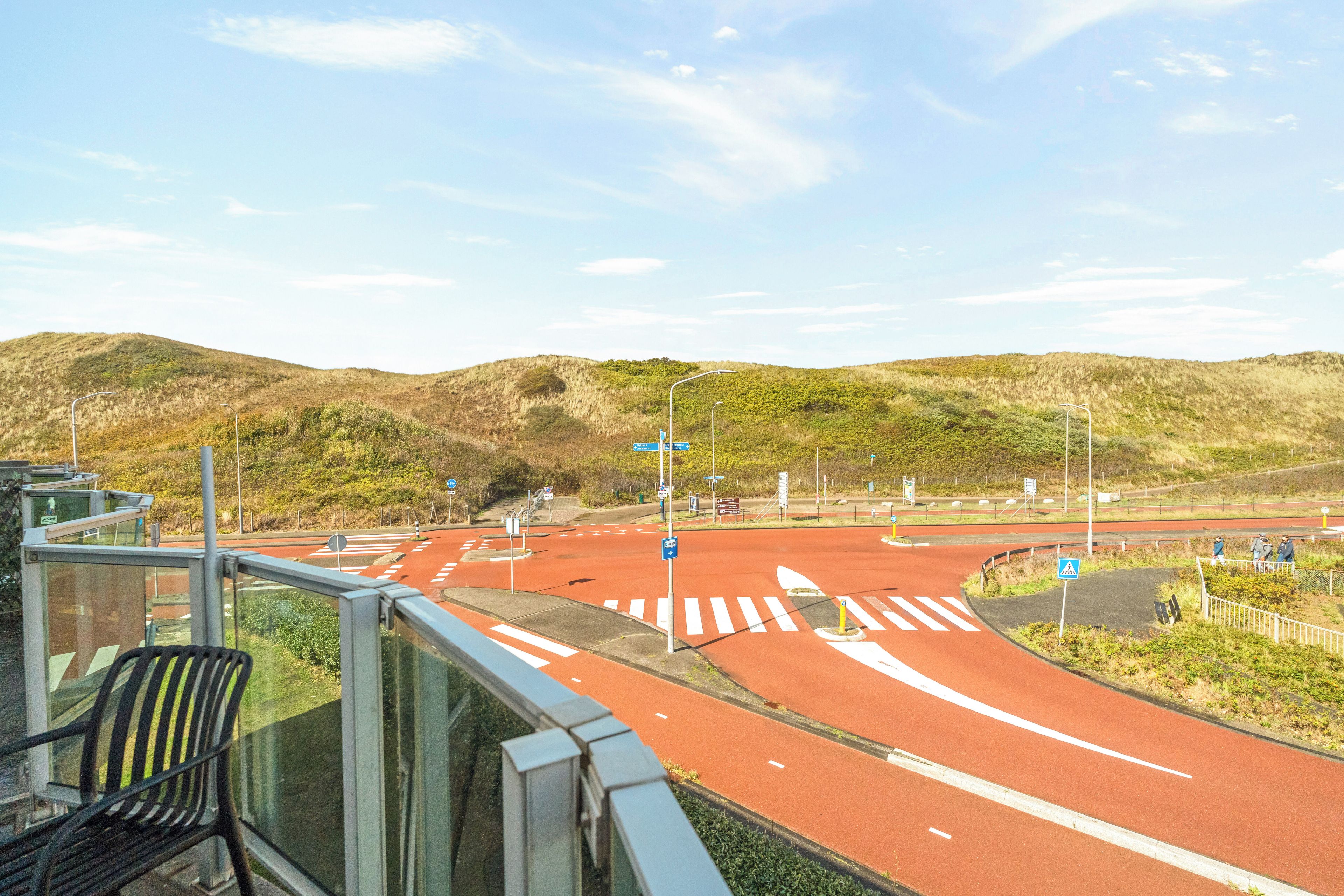 A multi-lane road with a red bike lane, pedestrian crossings, and a hill in the background.