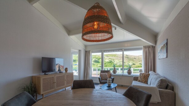 Ein modernes Wohnzimmer mit Esstisch, Sofa, Fernseher und großen Fenstern mit Blick.