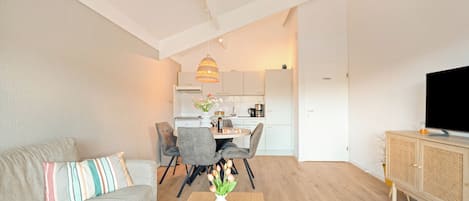 A modern living room with a sofa, coffee table, and a dining area with chairs and a kitchen in the background.