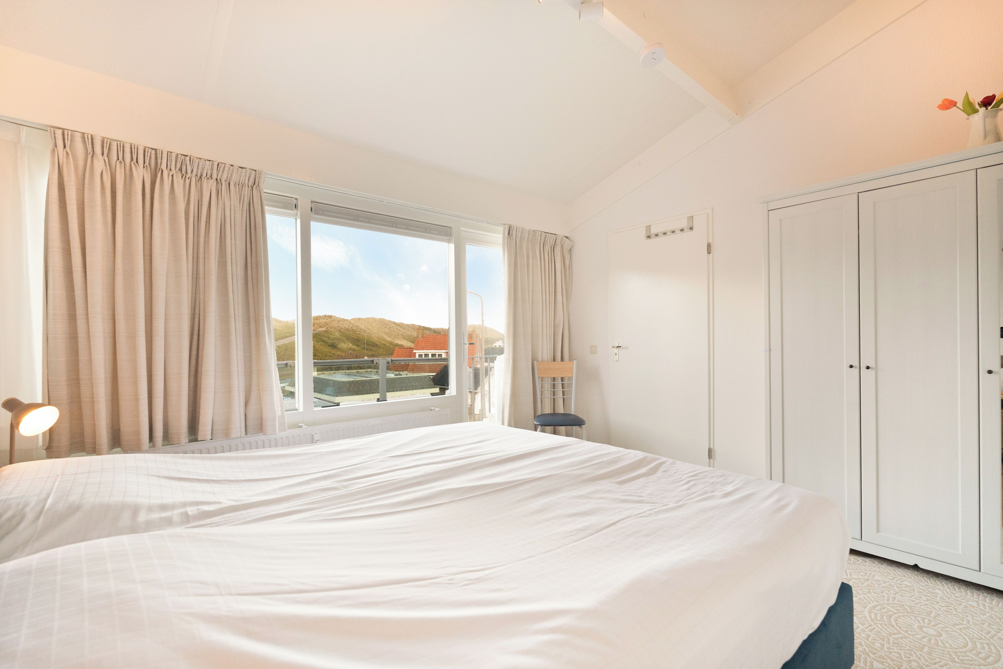 A hotel room with a large bed, a chair, a desk, and a wardrobe.