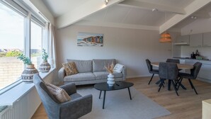 Ein modernes Wohnzimmer mit Sofa, Couchtisch und Esstisch. An der Wand hängt ein Gemälde und es gibt ein Fenster mit Vorhängen.