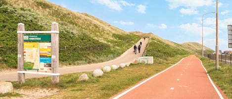 Un chemin pavé, agrémenté d’un panneau indicateur, des collines verdoyantes et un ciel dégagé.