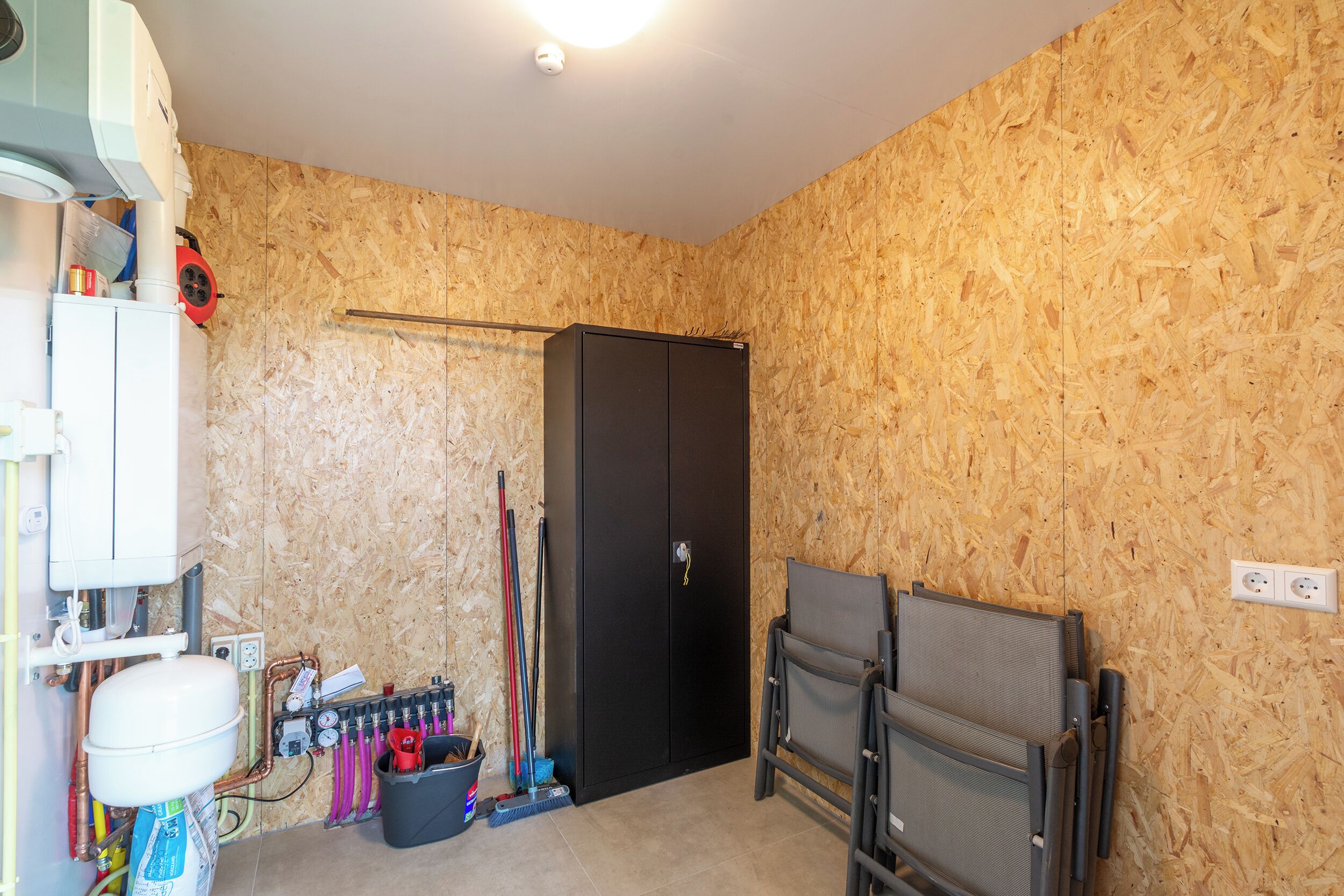 Une pièce avec une armoire noire, un radiateur blanc et une chaise noire.