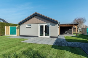 A residential building with a garage, a covered patio, and a well-maintained lawn. - Luxury Wellness Villa for 2 People (Julianadorp)