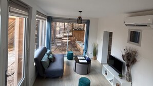 A modern living room with a sofa, ottoman, TV, and a sliding glass door leading to an outdoor patio. - L'Authentique Aparthotel: Charming Accommodations in Brive (Brive-la-Gaillarde)