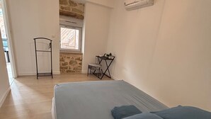 A bedroom with a bed, a small table with chairs, a window, and a stone wall. - L'Authentique Aparthotel: Charming Accommodations in Brive (Brive-la-Gaillarde)