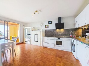 A modern kitchen with white cabinetry, a built-in oven, a washing machine, and a dining area with a table and chairs. - L'Acropole by Interhome (Cap d'Agde)