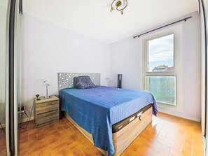 A bedroom with a bed, a nightstand, a heater, a window with a view, and a ceiling light fixture. - L'Acropole by Interhome (Cap d'Agde)