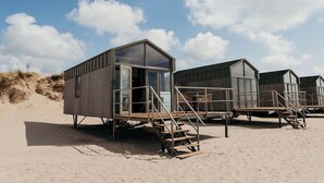 Een rij strandhutten met houten gevels en glazen deuren, elk voorzien van een trap die uitkomt op een houten terras.