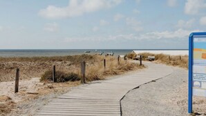 Een houten looppad naar het strand, met een bordje aan de rechterkant.