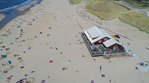 Uma praia com um edifício grande, provavelmente um restaurante ou bar, com telhado plano e uma placa.