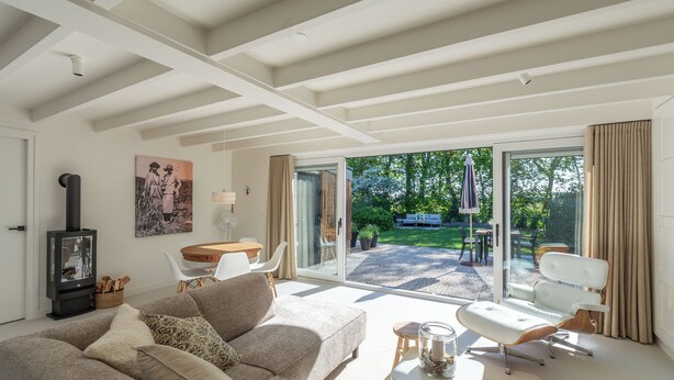 Ein modernes Wohnzimmer mit einer Couch, einem kleinen Tisch, einem Sessel, einem Kamin und Blick ins Freie.