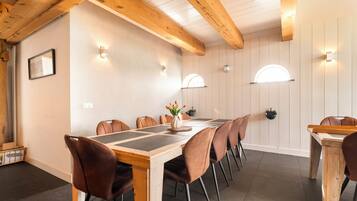 A dining area with a long wooden table, brown chairs, and wall-mounted light fixtures.