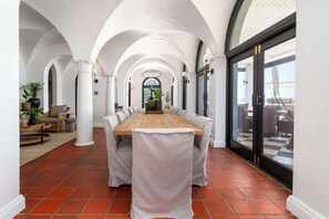 Un vaste espace dédié à la salle à manger, avec une longue table en bois, des chaises blanches et une vue dégagée grâce à une grande porte vitrée.