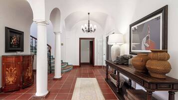 Un vaste hall d’entrée avec des colonnes blanches, un lustre, une console en bois agrémentée d’objets décoratifs et un tableau encadré au mur.